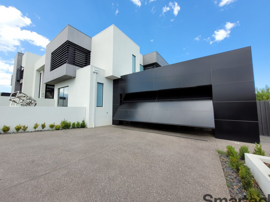 beautiful two storey home with a custom garage, smartech tilt door opening, clad in large black panels.