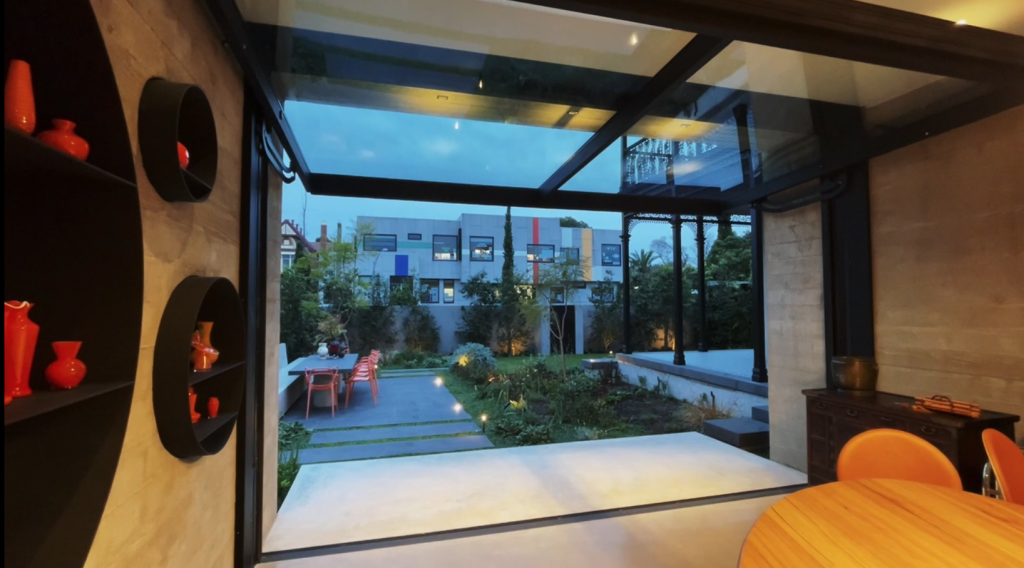 a glazed open wall open to a beautiful backyard in the early evening