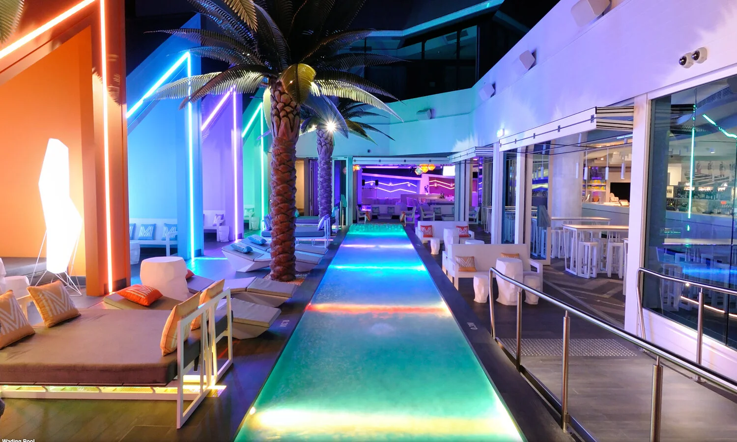 Matisse Beach Club at night with their multi-colored pool deck featuring a beautiful Bar viewable through multiple large glazed folding doors.