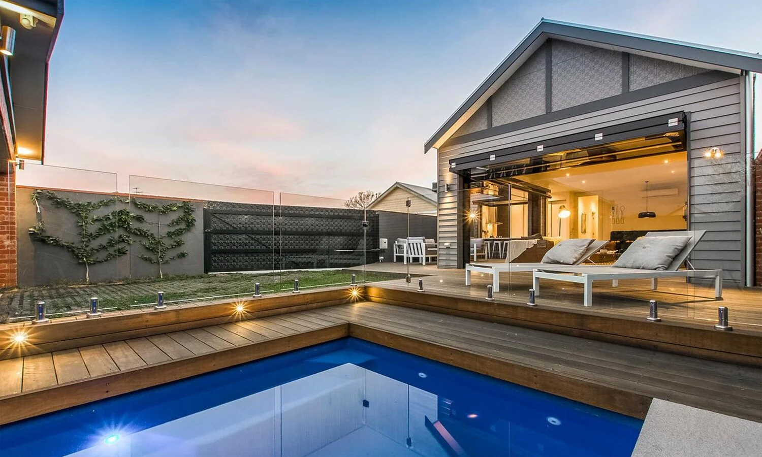 A deep dark blue pool backed onto a beautiful wooden deck with an open glazed folding door.