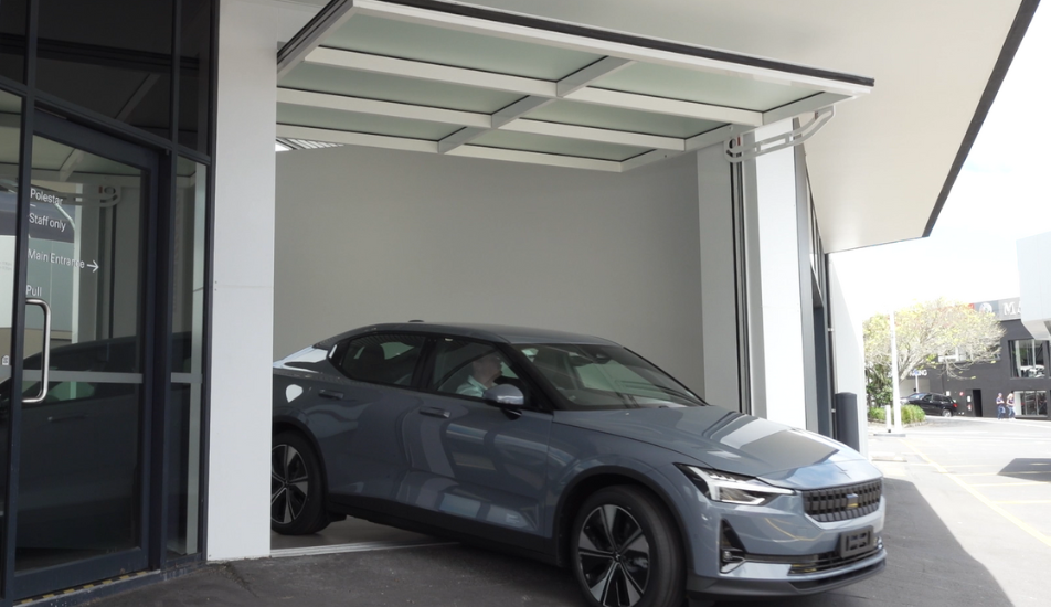 Polestar 2 Car leaving the showroom through the open tilt door on a bright sunlit day.