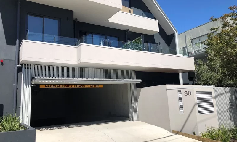 Modern apartment building with a garage entrance, featuring a facade with vertical slats and a height clearance sign of 2.1 meters.